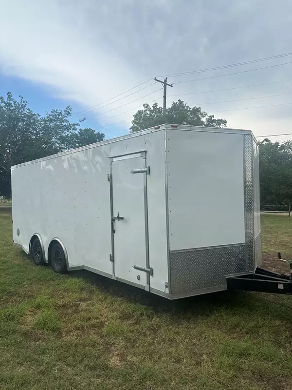 A 20ft white enclosed cargo trailer with dual axles on grass