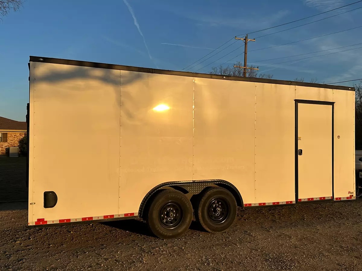 A 20ft beige enclosed cargo trailer with dual axles on gravel